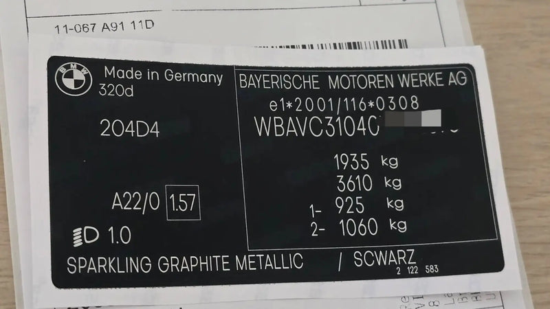 Black bmw 320d vehicle identification plate with silver metallic lettering and the ’made in germany’ designation.