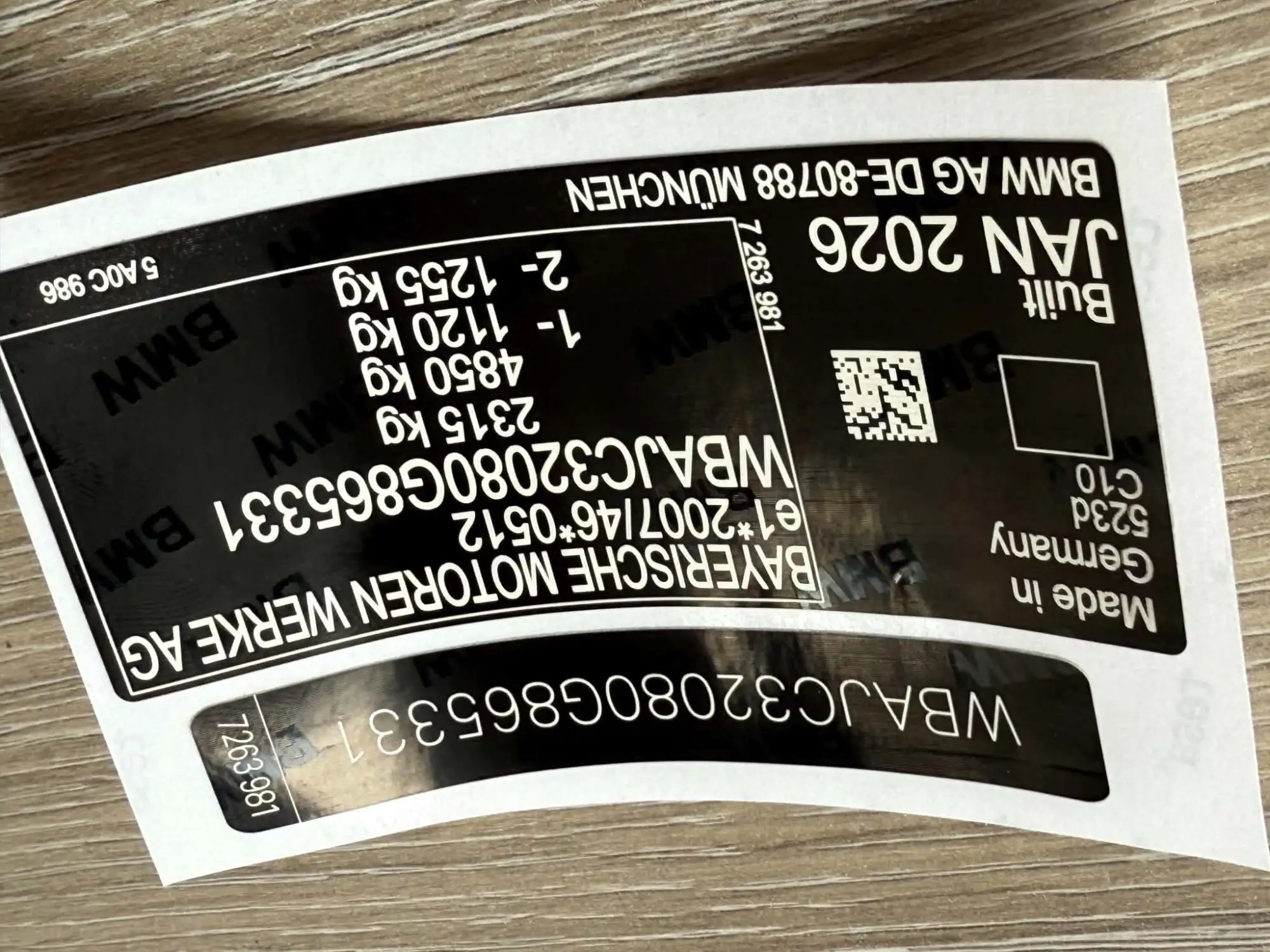 Black bmw vehicle identification label with white text and a qr code, indicating it was built in germany.