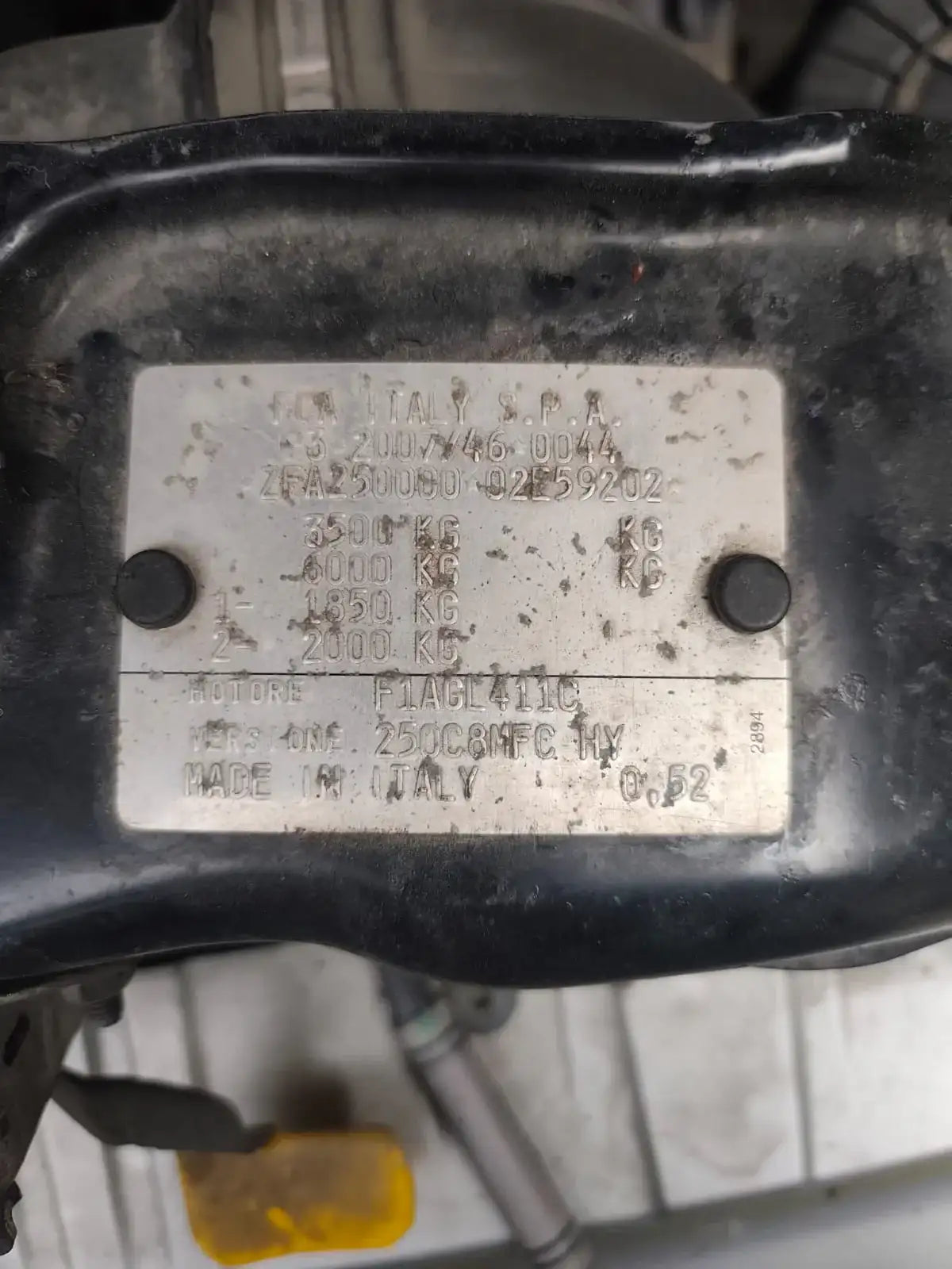 Black plastic engine cover with a silver metal plate bearing engraved text and numbers.