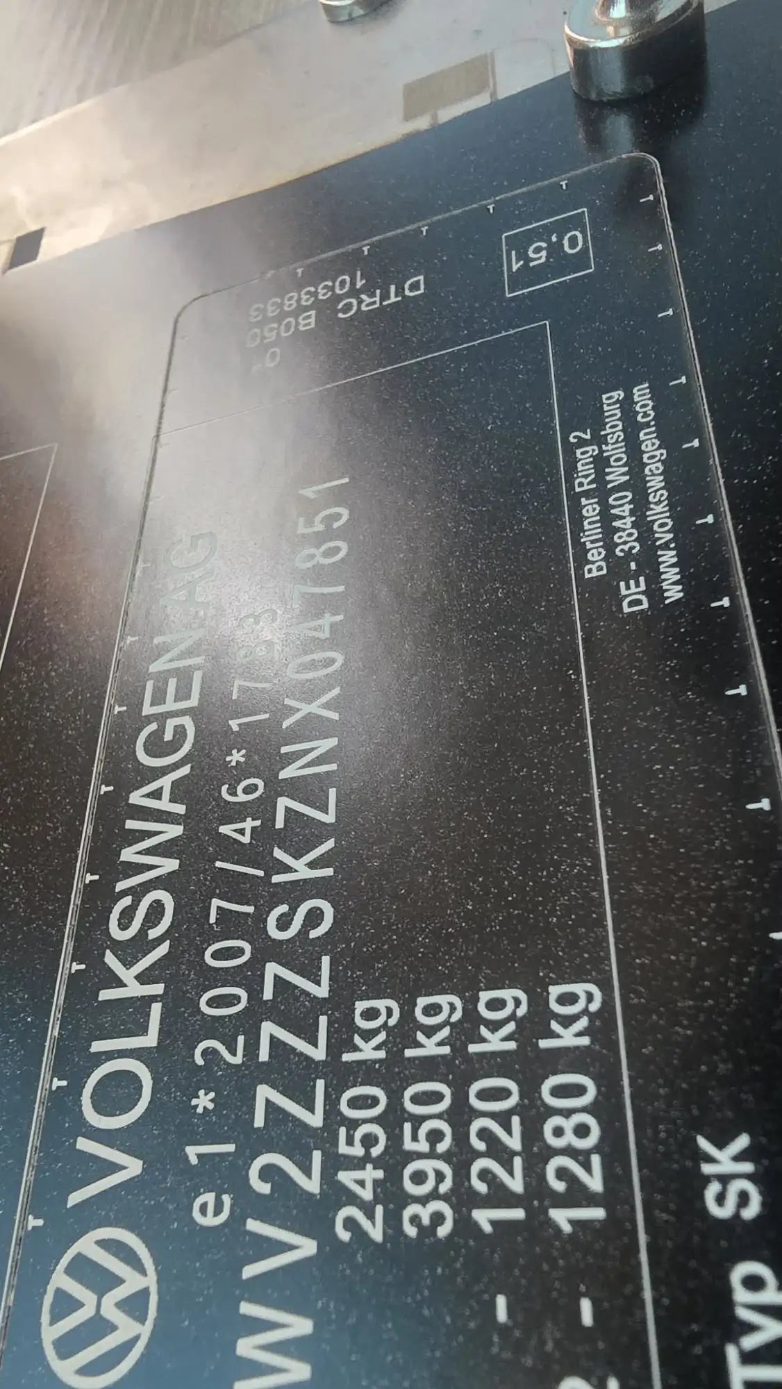 Black volkswagen vehicle identification plate with white engraved text and logo.